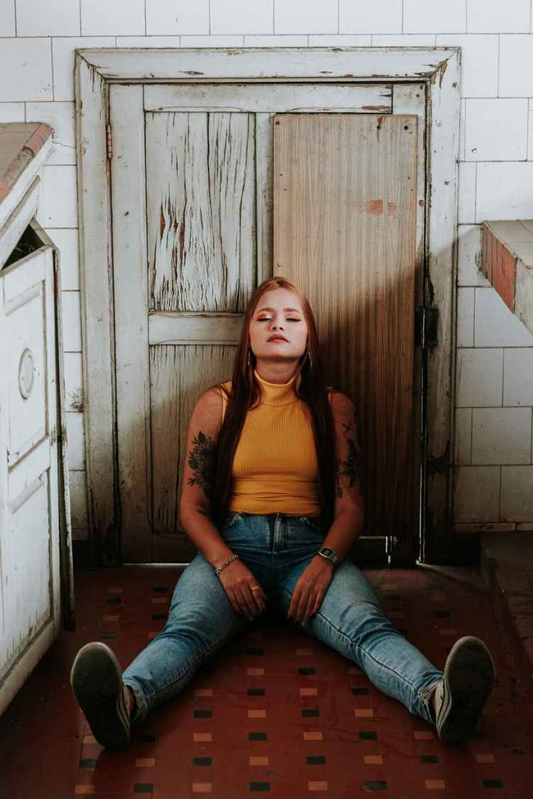woman in orange tank top and blue denim jeans sitting on floor